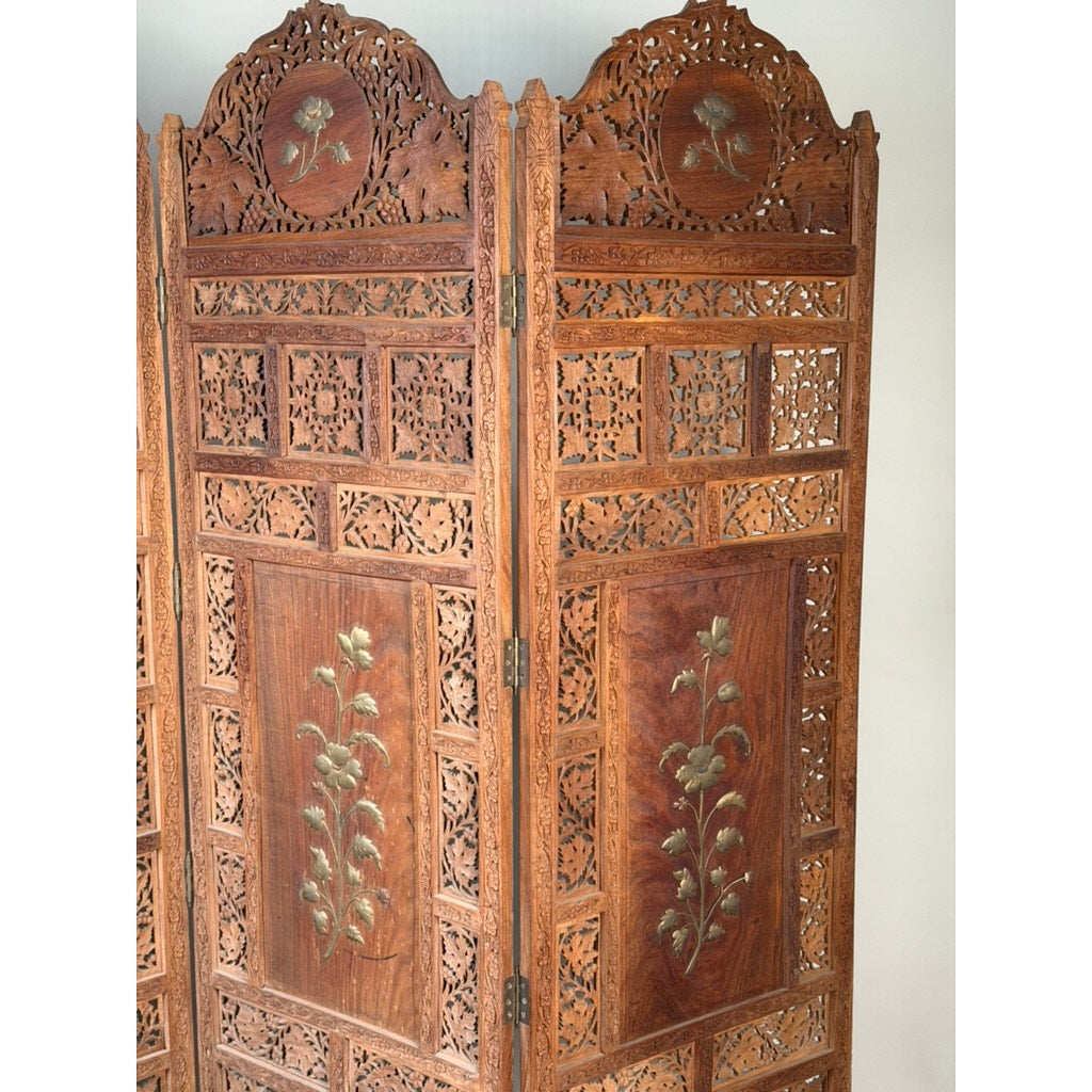 Introducing the Early 20th Century Anglo-Indian Carved Teak Four-Panel Screen with Applied Brass Floral Decoration from Pearl City Antiques. This exquisite antique room divider features four finely crafted teak panels, each adorned with intricate carved patterns and elegant applied brass floral motifs. The handcrafted design showcases detailed cut-out work and a polished finish, capturing the timeless elegance of traditional Anglo-Indian folding screens.