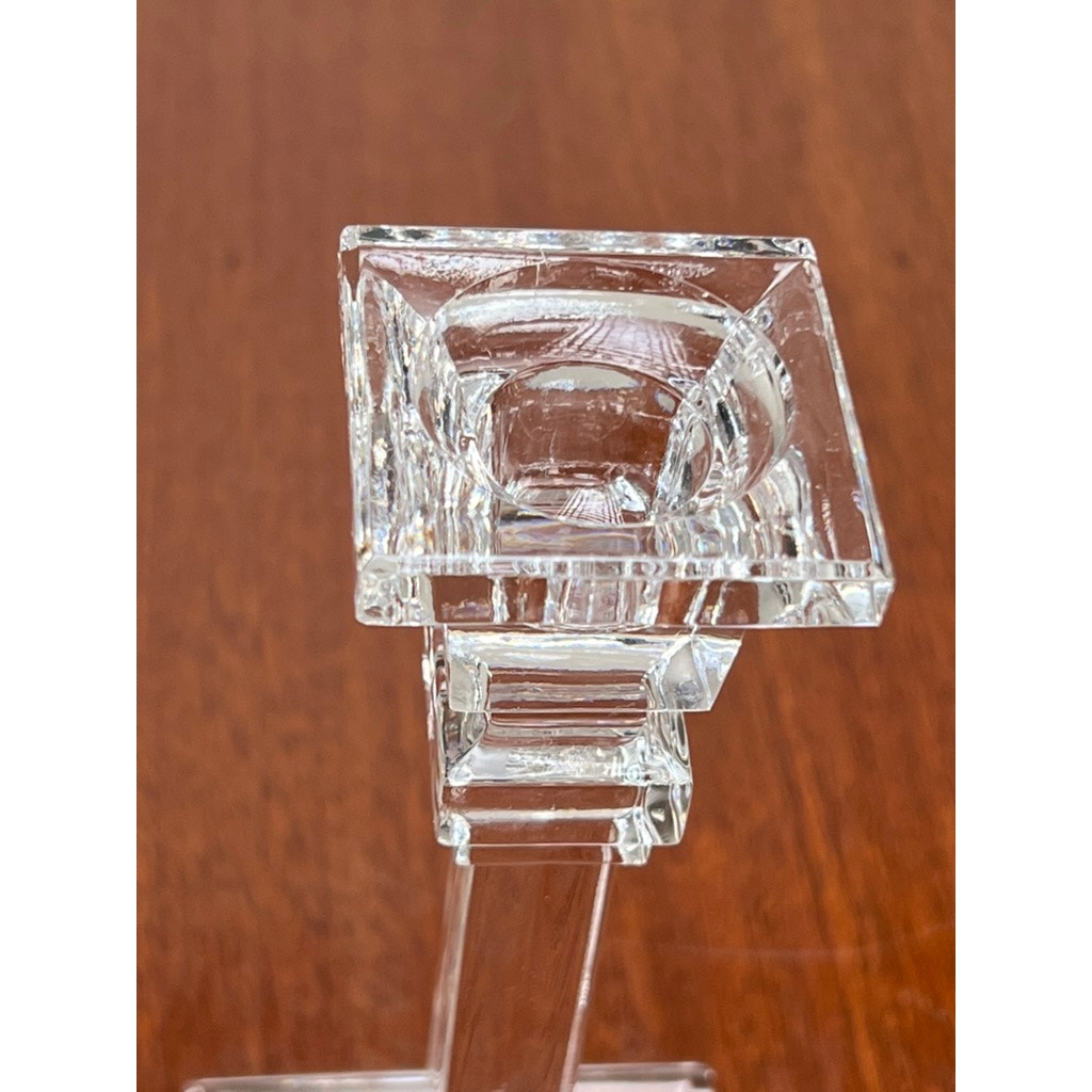 A close-up of a clear, square glass candlestick holder by Tiffany & Co. rests on wood, its geometric lines and reflections echoing the vintage charm of the Vintage Pair Tiffany & Co Clear Crystal Candlesticks.