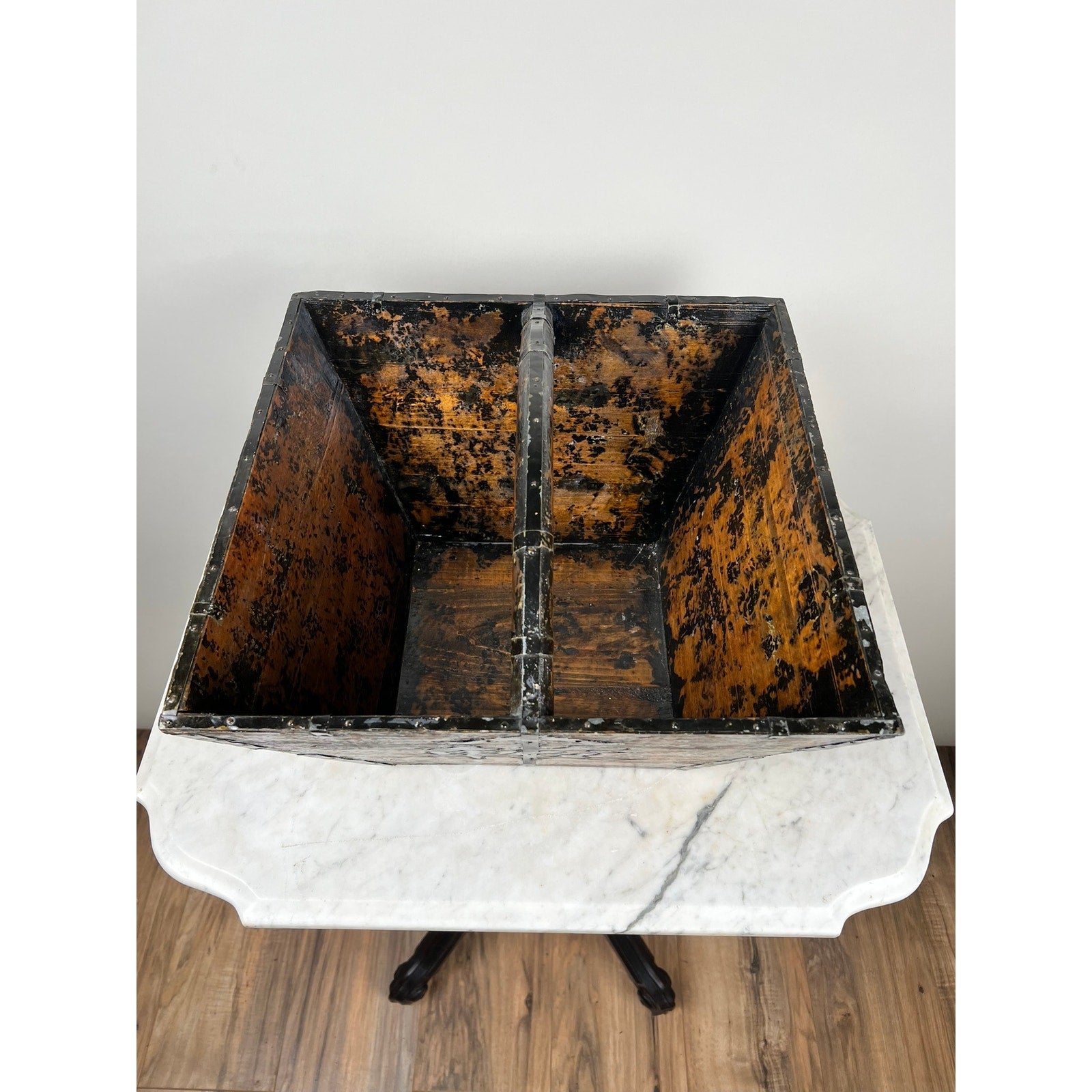 An Antique Chinese Elm Dou Rice Measure, likely mid-19th century from Shanxi, with faded orange and black paint and a central divider, sits open on a white marble-topped table with a dark wooden base against a pale wall.