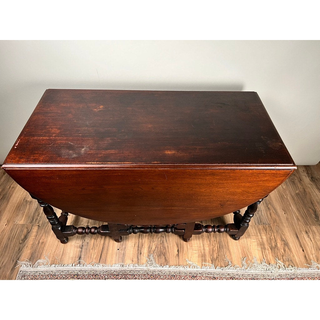 An Antique English William & Mary Walnut One Drawer Gateleg Dining Table (Early 18th Century) with turned legs, rectangular form with both leaves down, sits on a wood floor by a rug, showcasing classic early English style. Brand unknown.
