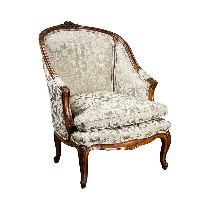 Antique French Louis XV Rococo style bergère arm chair, mid 19th century, with curved legs, ornate carved walnut frame, and newer light-colored damask upholstery featuring an intricate floral pattern. Brand unknown.