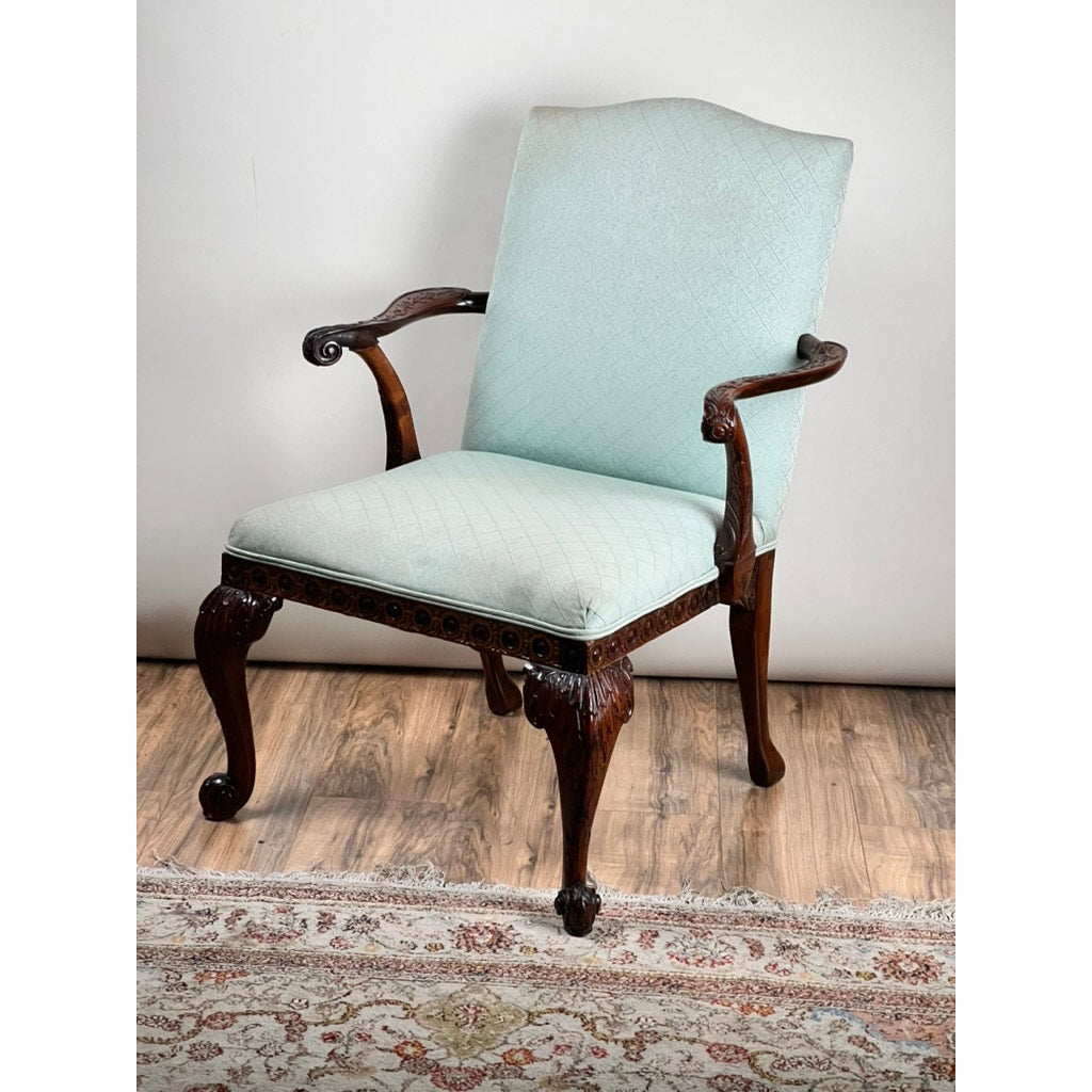 An Antique George II Mahogany Gainsborough Open Arm Chair (c. Mid 19th Century) with light blue upholstery and cabriole legs sits on a hardwood floor beside a patterned rug. Brand: Unknown.