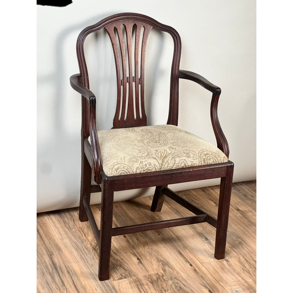 An Antique English George III Mahogany Hepplewhite Armchair (early 19th century) with a decorative curved backrest and light-patterned upholstered seat is shown on a wood floor against a plain, light background.