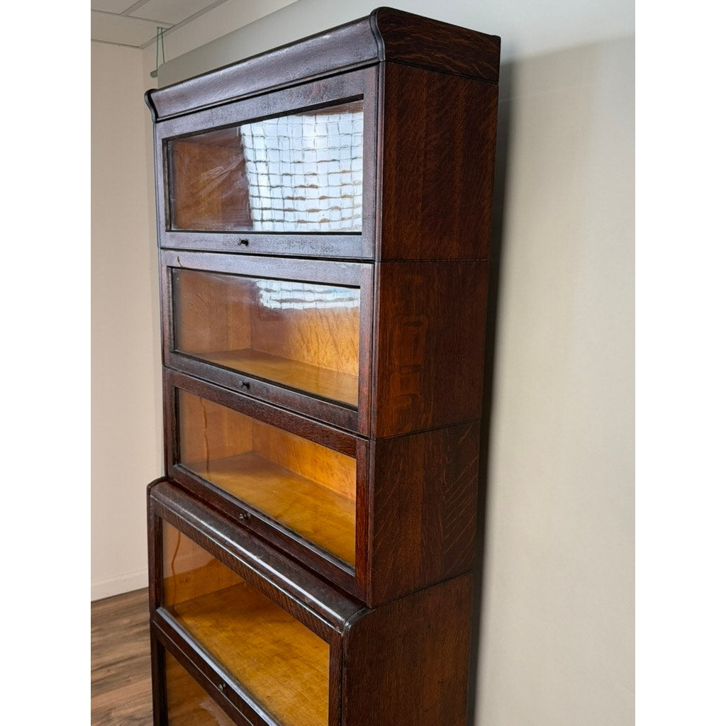 A tall, dark quarter-sawn oak barrister bookcase by Camden Cabinet Company, c. 1910, with five stacked sections—each featuring a glass-front door—is set against a white wall on a wooden floor.