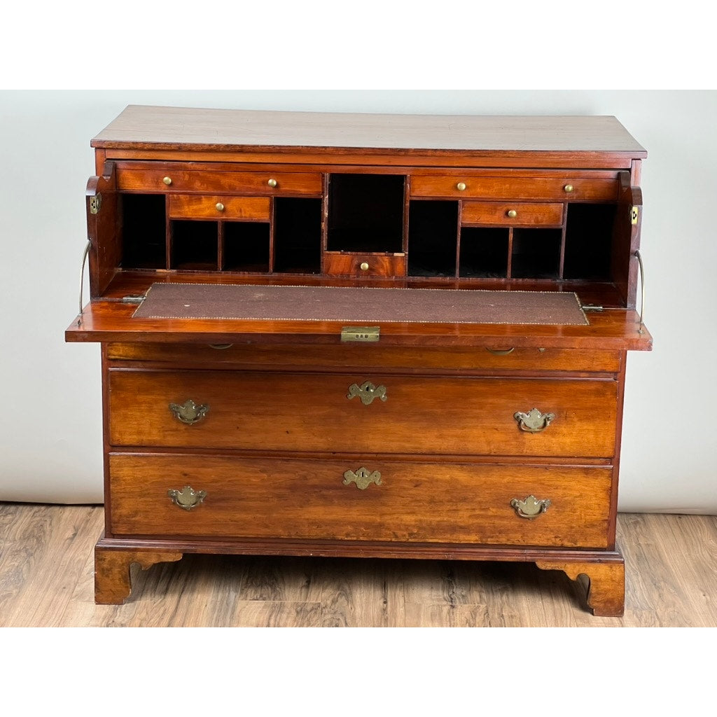 An Antique George IV Butlers Secretary from the early 19th century, featuring three large drawers and a fold-down writing surface with interior cubbies and drawers, stands on a wood floor against a light wall. Brand: Unknown.
