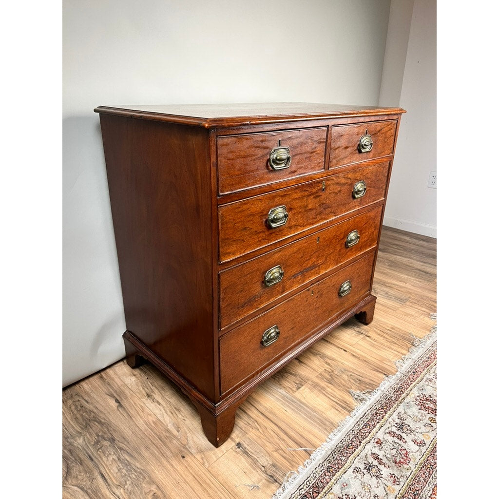 The Late Georgian English Mahogany Chest of Drawers, Circa 1780–1810, sits gracefully on a wooden floor beside a patterned rug and a white wall; this refined antique exemplifies period furniture from the late Georgian era.