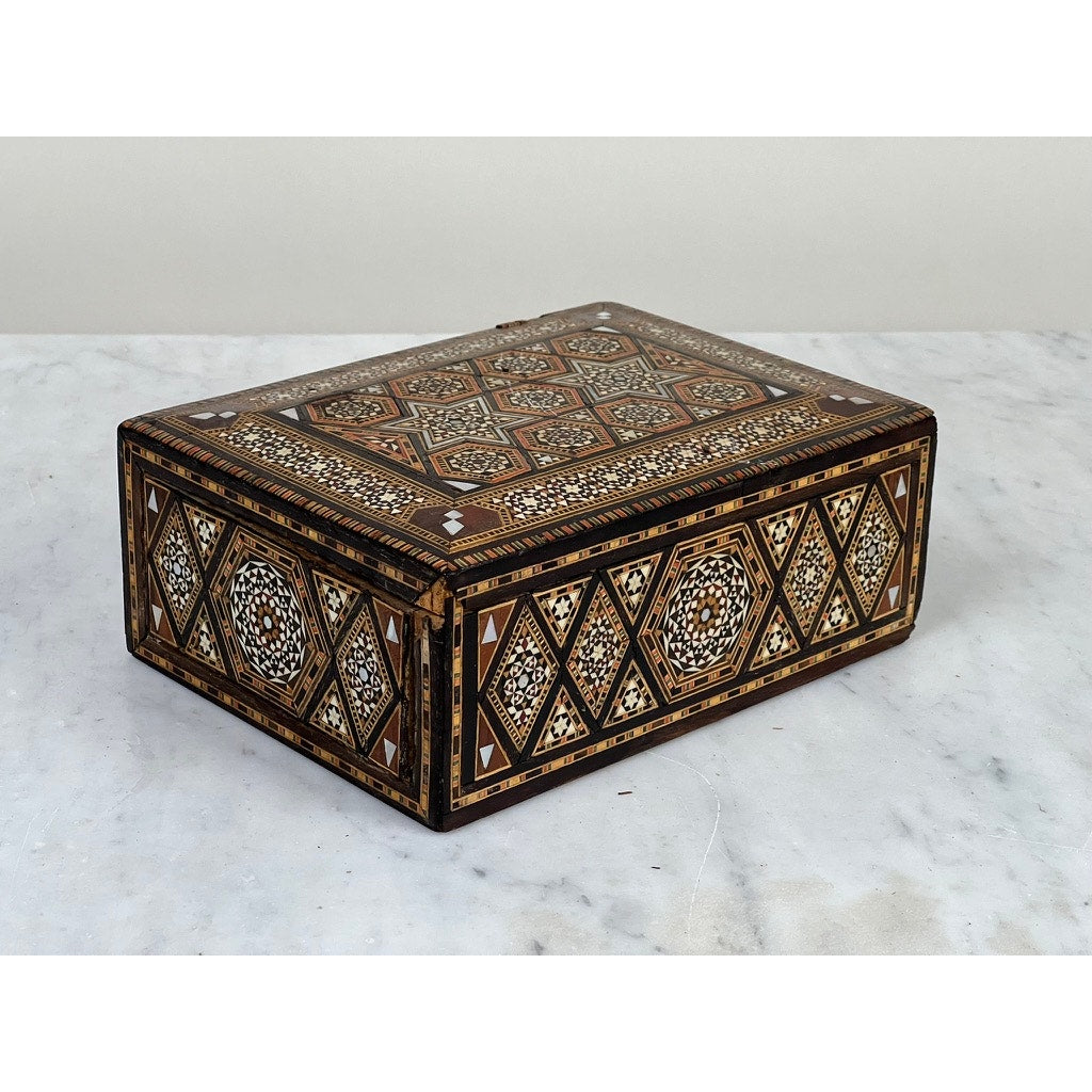 An Antique Persian (likely Syrian) Khatam inlaid wood jewelry box, late 19th century, with brown, black, and white star and diamond motifs on its rectangular sides and top, shown on a light marble surface.