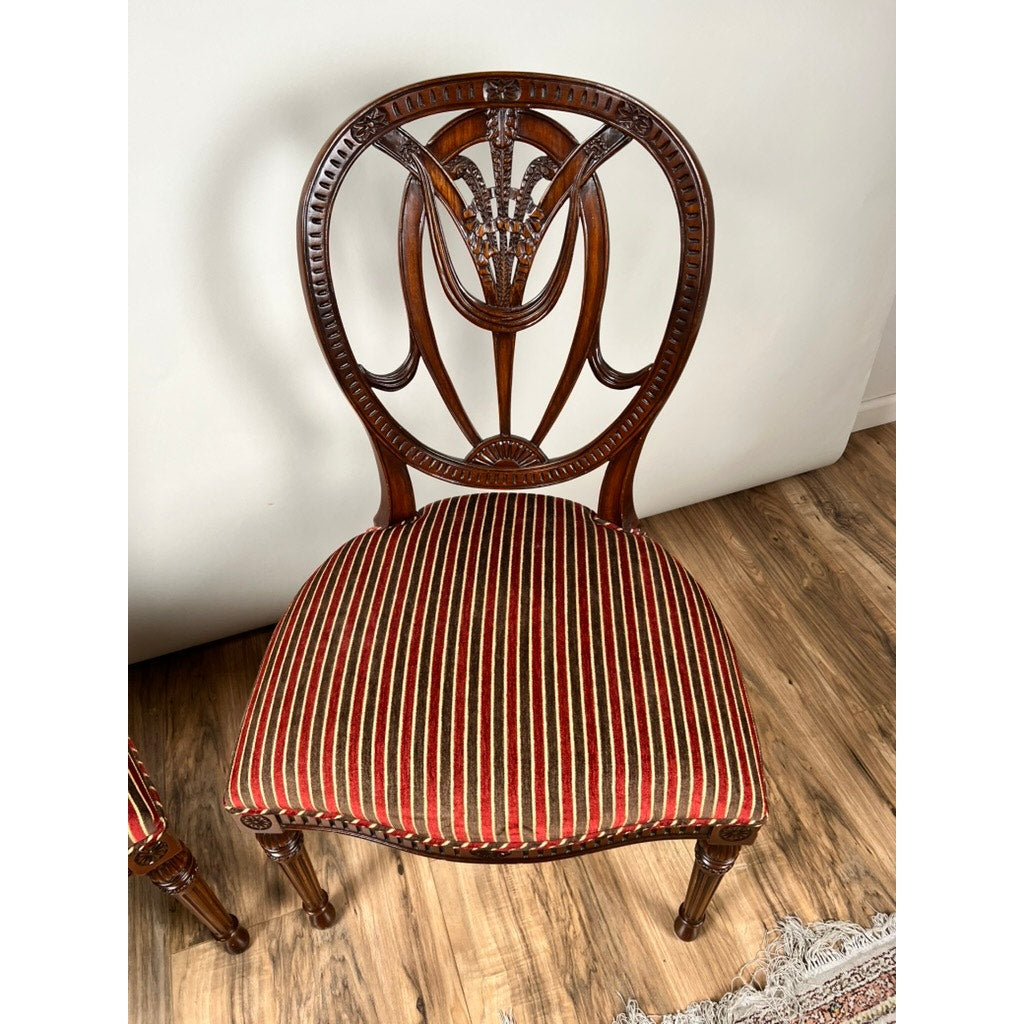 A Vintage Pair Wheel Back Side Chairs by Ardley Hall, featuring ornate carving and a cushioned seat in red, black, and white stripes, are set on a wooden floor against a white wall.