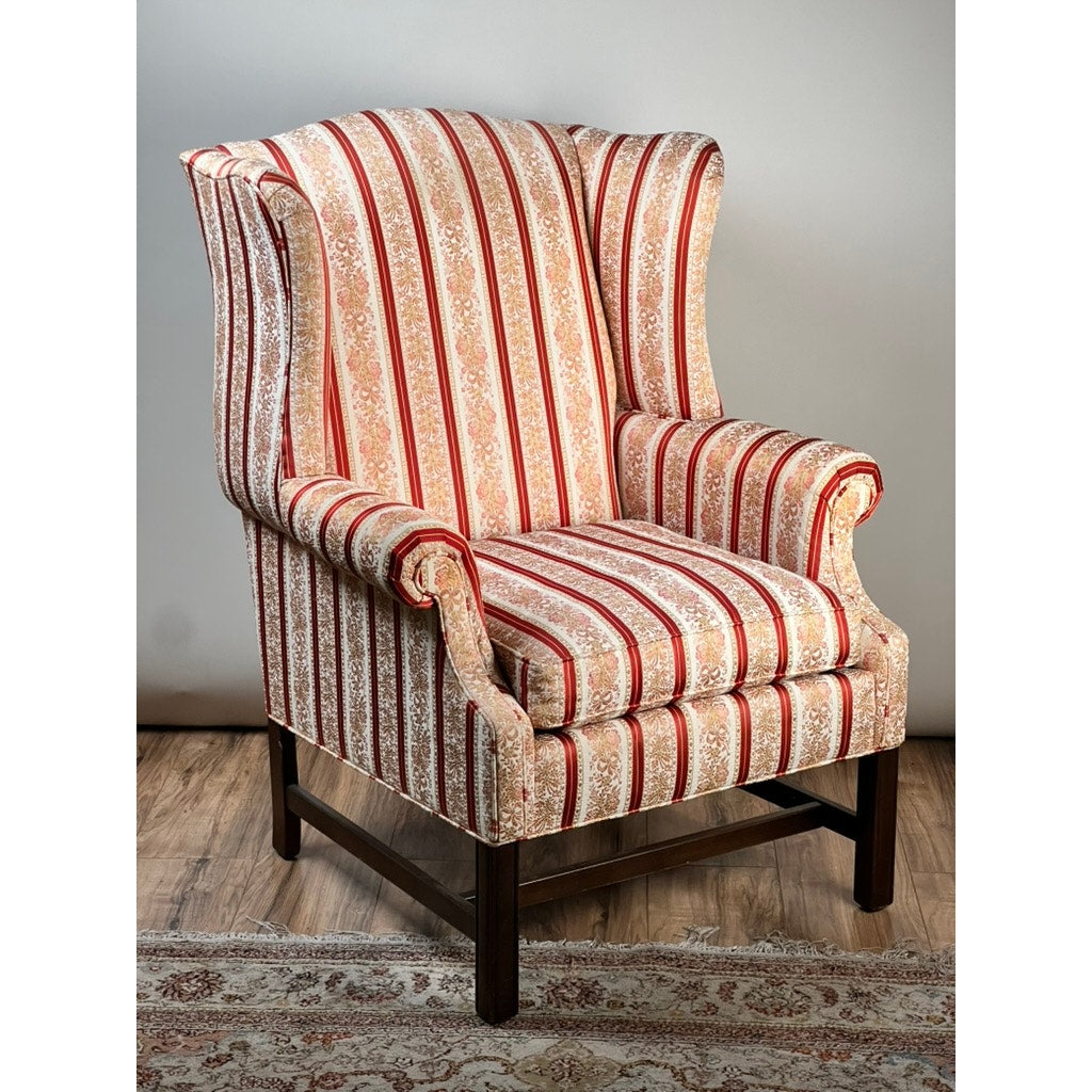 The Vintage Chippendale Style Wingback Chair by Ethan Allen features classic striped upholstery and floral patterns. Set on wooden legs, this piece rests on a light patterned rug and wooden floor against a plain wall.