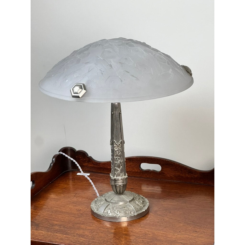 A Vintage French Art Deco Frosted Glass Table Lamp by Muller Frères Lunéville c. 1920, featuring a dome shade and ornate metal base, is displayed on a wooden tray-style table against a plain white wall.