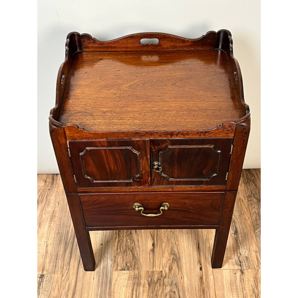 An Antique George III Bedside Commode from the late 18th century, this mahogany piece features a pull-out leather surface, cabinet doors, a lower drawer with brass handle, and classic straight legs for timeless Georgian charm. Brand unknown.