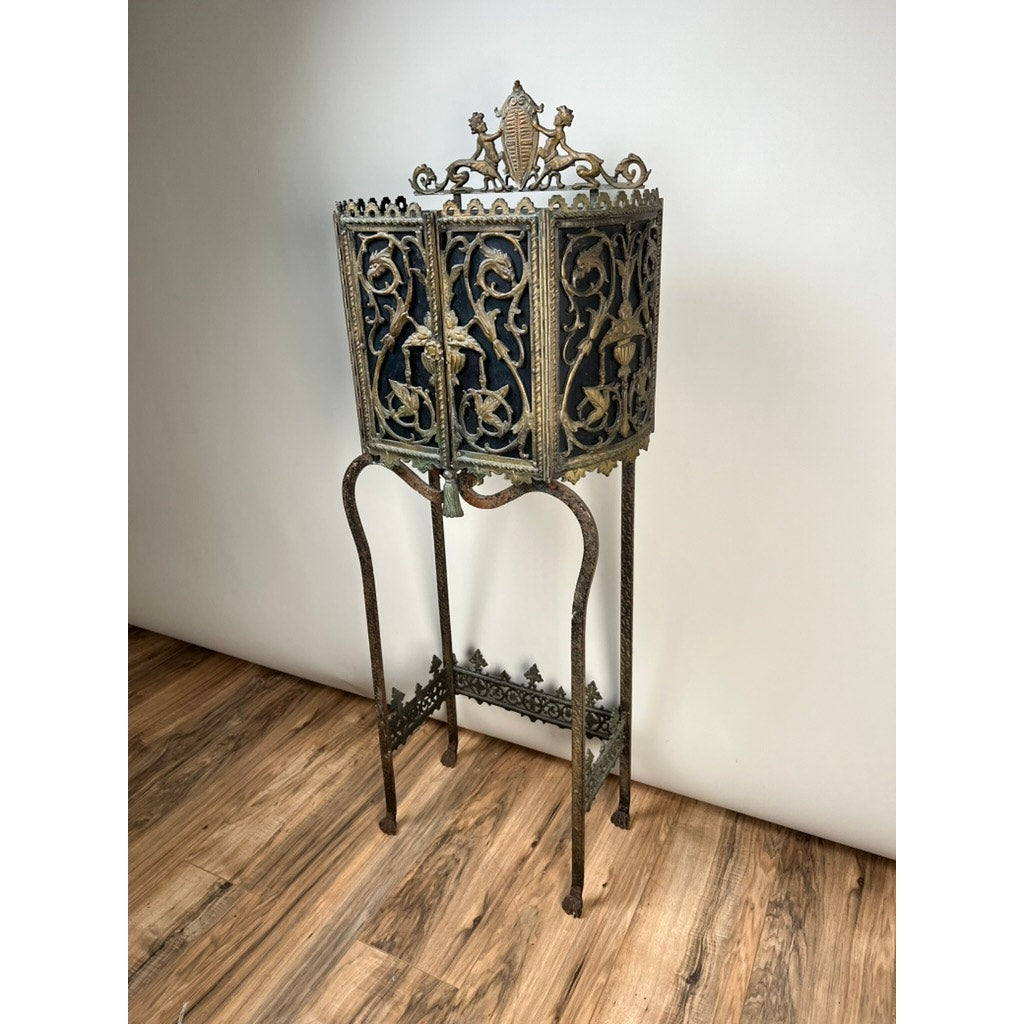 Antique Gothic Revival cast iron and brass phone stand, attributed to Oscar Bach or Bertram Segar c.1920, features intricate floral and vine designs, a decorative crest, and stands on curved legs against a plain white wall.