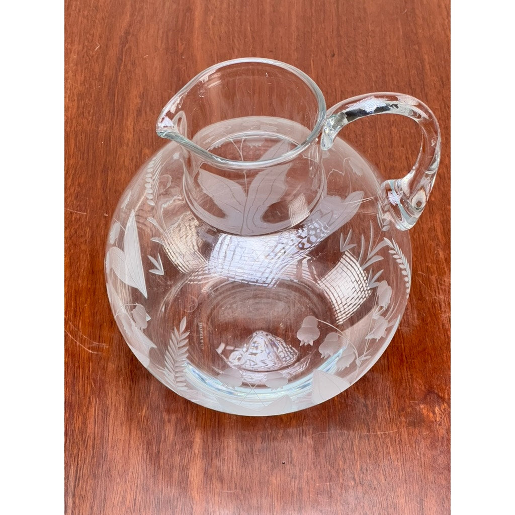 A Vintage Tiffany & Co. etched crystal pitcher with a delicate lily of the valley floral motif stands on a wooden surface.