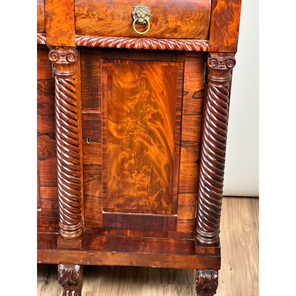 Close-up of an Antique American Empire Mahogany Sideboard, probably Philadelphia c. 1840, featuring rosewood edge banding, ornate columns, claw feet, brass lion’s head drawer pull, and a glossy finish that highlights the wood’s rich grain.