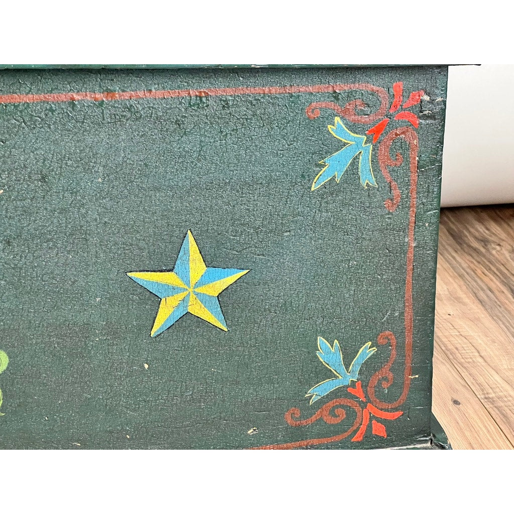 Close-up of an Antique Paint Decorated English Sea Chest c. Late 19th Century, featuring worn green paint with a yellow and blue central star, red and blue corner motifs, and a thin red border. Brand: None/Unknown.