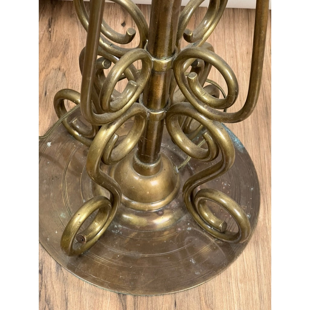 A close-up of the circular, ornate brass base of an Antique Art Nouveau Brass Floor Lamp attributed to Jules Cayette and Charles Schneider c. 1920, with spiraled metalwork and visible scuffs on a wood floor. Brand: Unknown.