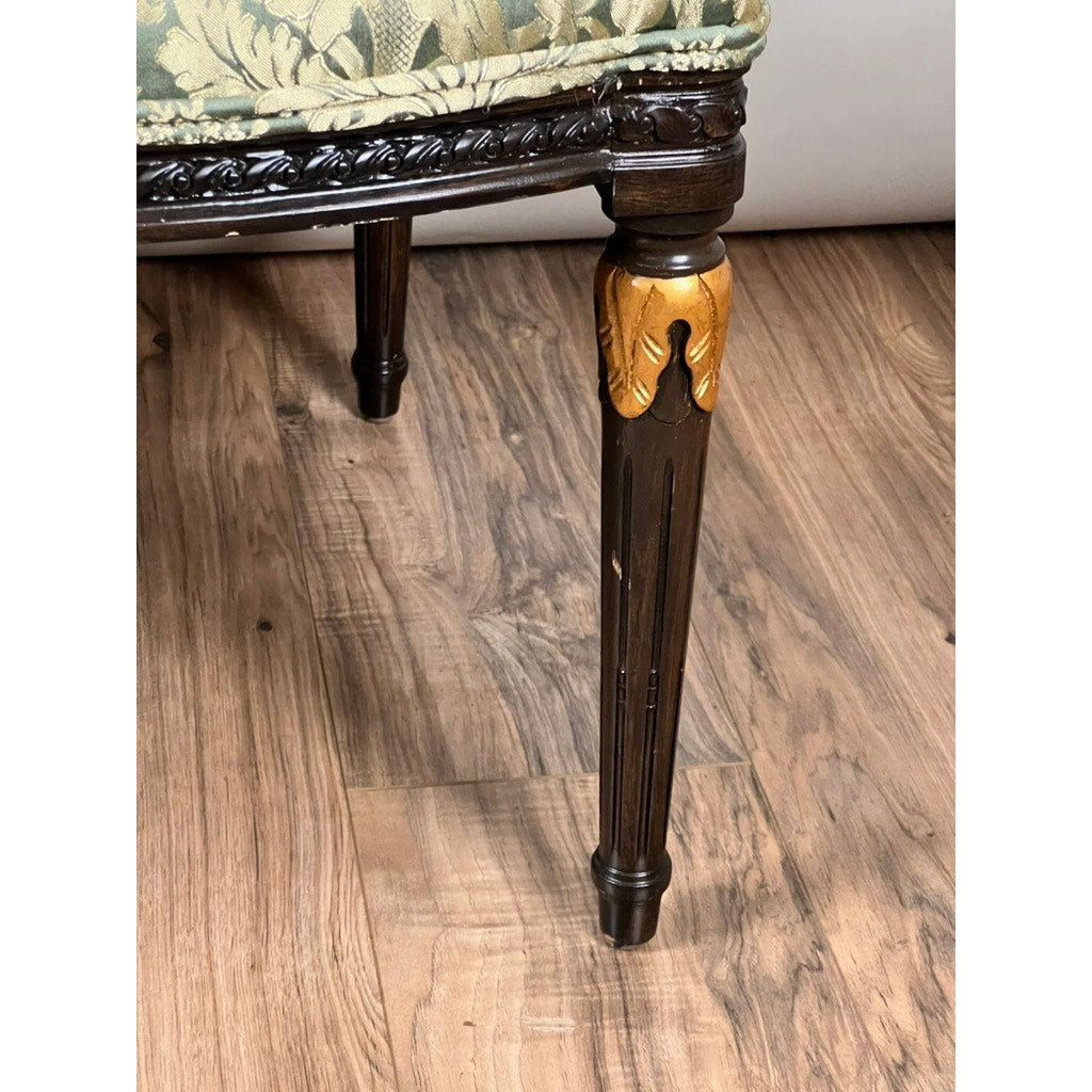 Close-up of a carved dark wood leg with gold leaf on a wood-patterned floor, from a Vintage Louis XVI Style Settee in green damask upholstery, evoking French neoclassical elegance. Brand: None/Unknown.