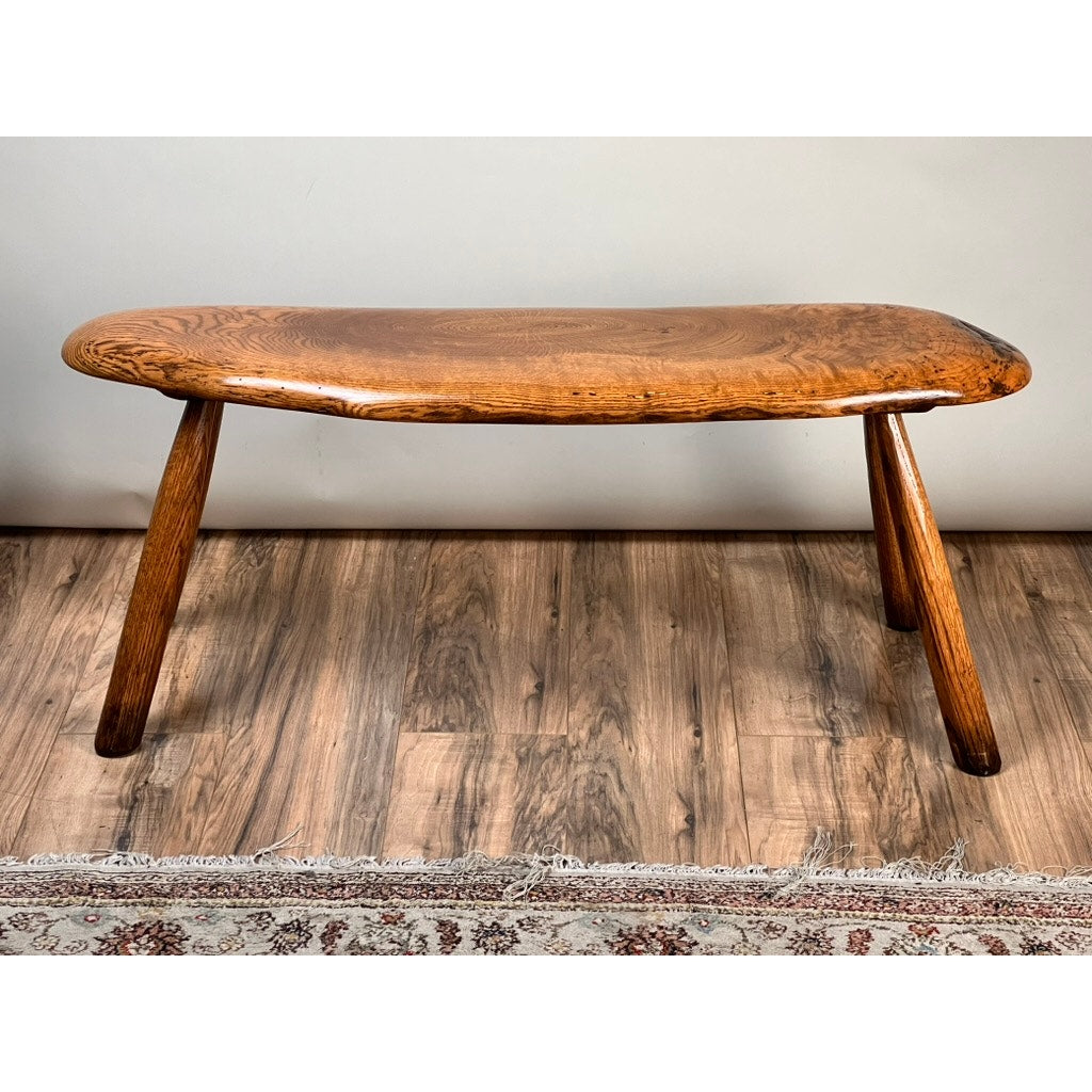 The Vintage Hand Made Oak Wabi Sabi Bench signed Neil Panyik has a smooth curved seat, three angled legs, and a rich polished finish. Its minimalist rustic design makes it a standout piece beside a patterned rug on hardwood floors.