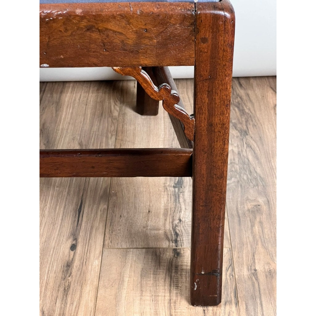 Close-up of an Antique Chippendale Walnut Open Arm Chair leg (c. Late 18th Century) showing scuffs and scratches on its carved support and rectangular form, displayed on a light brown wood floor. Brand: None/Unknown.