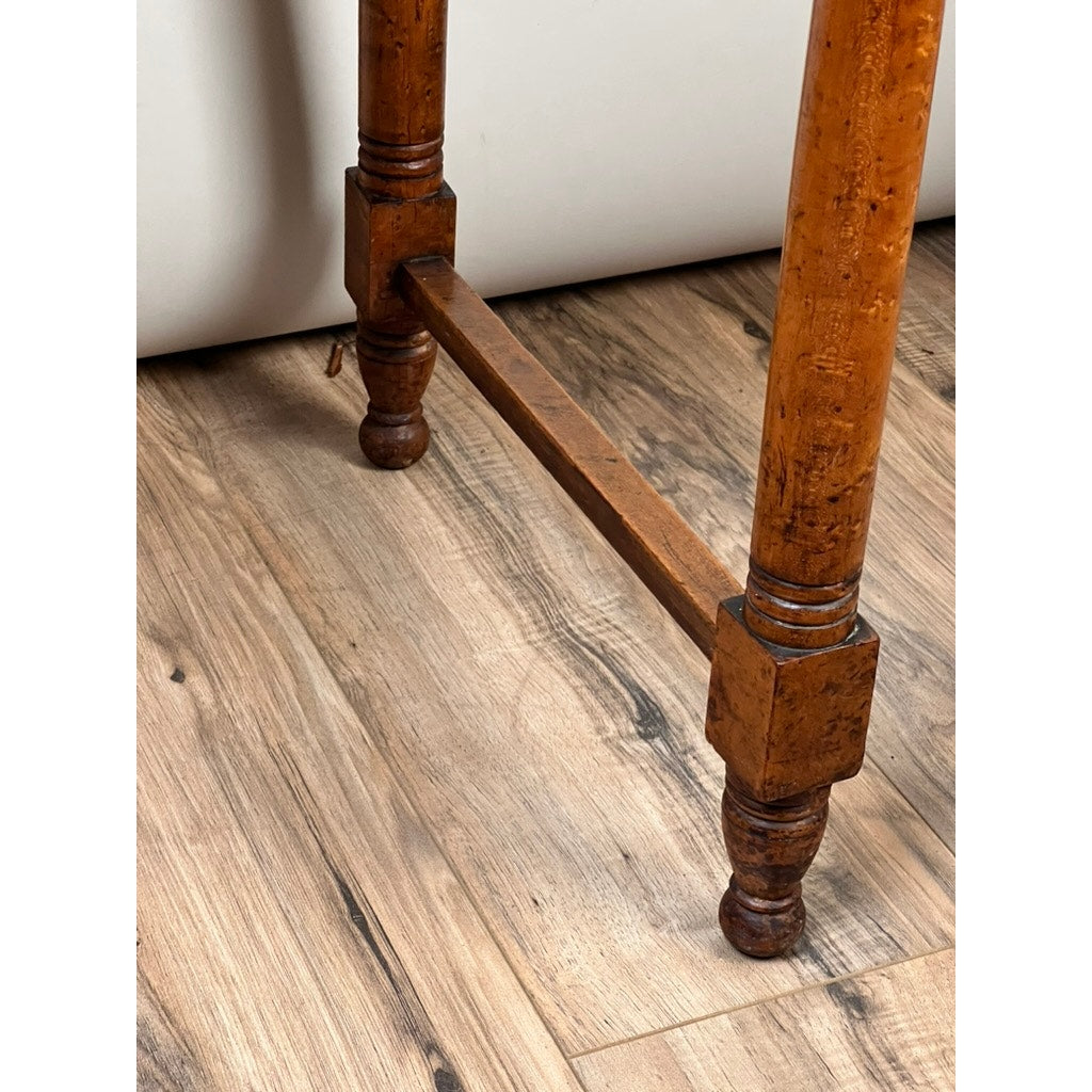 Close-up of two turned legs with a stretcher bar on a light brown wood floor. This Antique Sheraton Birdseye Maple One Drawer Stand, c. Early 19th Century, shows classic early American details near a white wall or furniture.