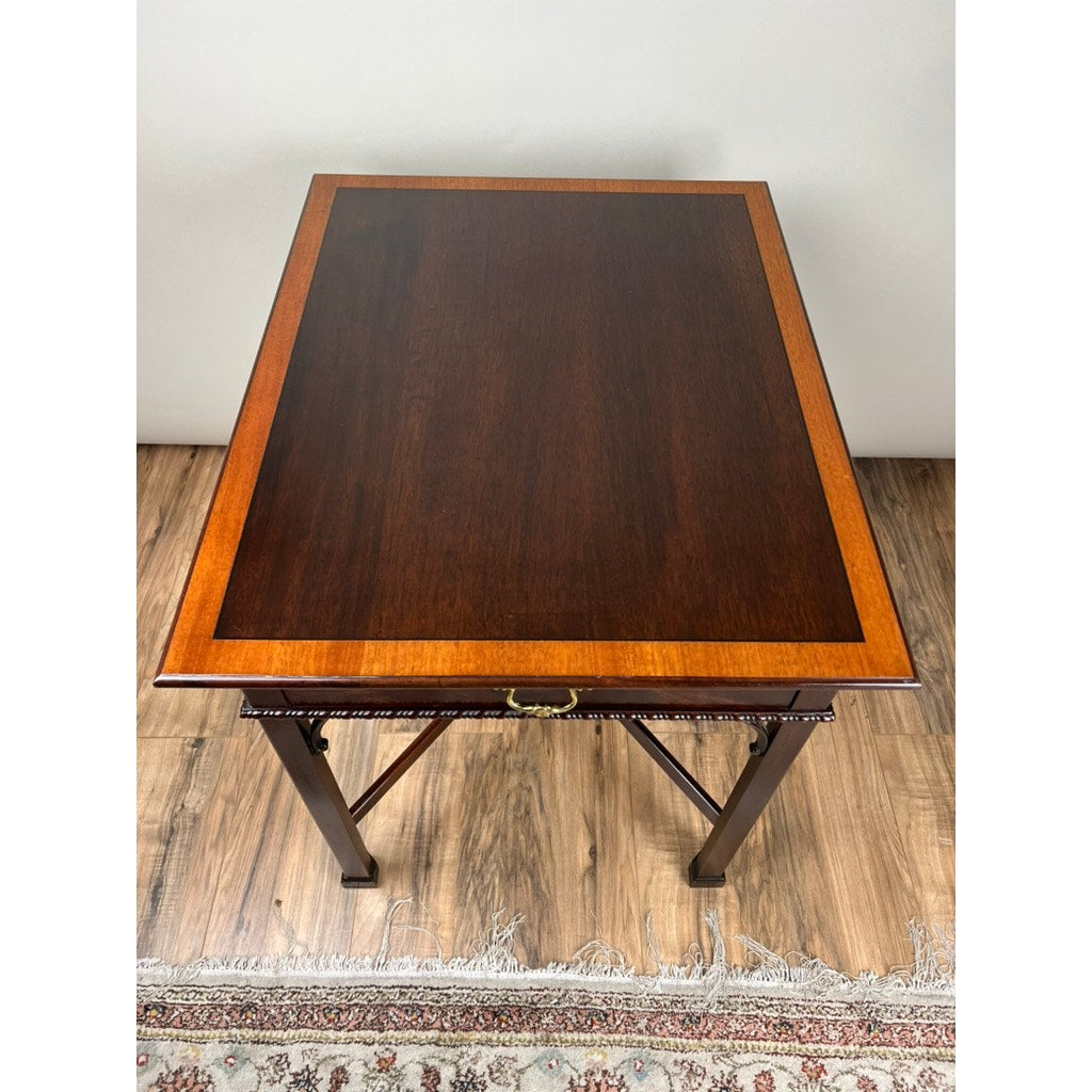 The Vintage Federal Style X Stretcher One Drawer End Table by Stickley features a dark central panel, lighter border, and brass handle, sitting on hardwood flooring with part of a patterned rug visible beneath.