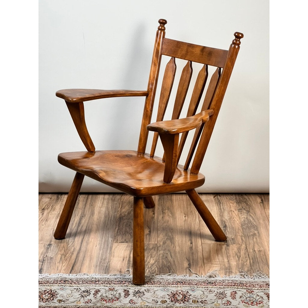 A Vintage Herman DeVries for Cushman No. 5-82 Rock Maple Easy Chair by Cushman sits on a wood floor near a patterned rug, positioned against a plain light-colored wall.
