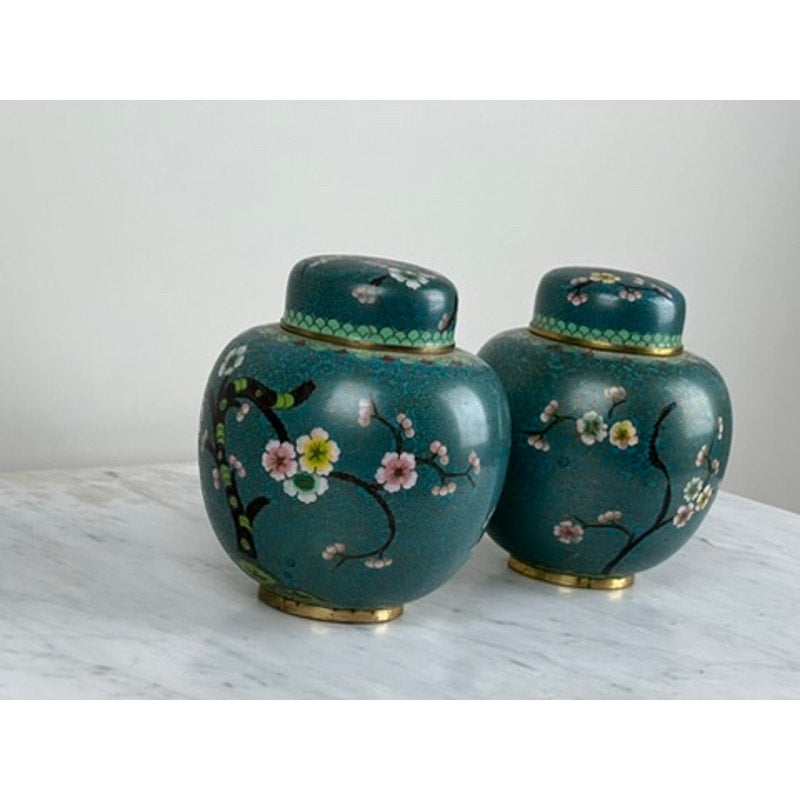 A Vintage Pair of Chinese Cloisonné Ginger Jars with green enamel, pink and white cherry blossoms, and gold accents adds Asian-inspired elegance to a white marble surface against a plain light background.