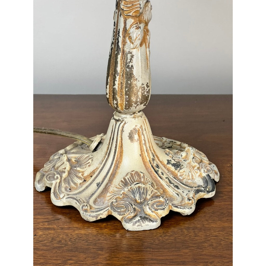 A close-up of a Vintage Art Nouveau Slag Glass Two-Light Table Lamp (c. 1935–1955) with a chipped white and gold base, on a wooden surface—a striking piece to enhance your decor with unique, decorative lighting. Brand: Unknown.