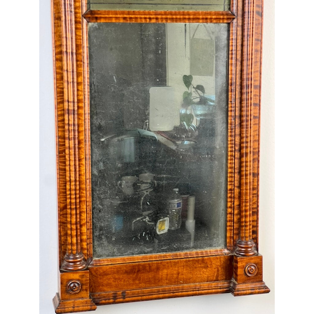The Fine Antique Federal Period Tiger Maple Two Panel Mirror c. 1820, with a slightly dusty surface, reflects a kitchen scene featuring a sink, kitchen items, and a plant in the background.