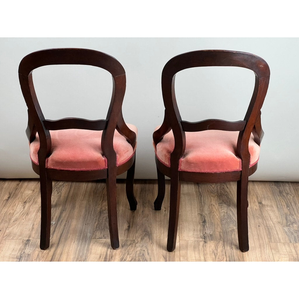 The Antique Pair Victorian Walnut Balloon Back Side Chairs, shown from behind on a wooden floor against a light wall, feature curved backs and vintage rose velvet upholstery. Brand is unknown.