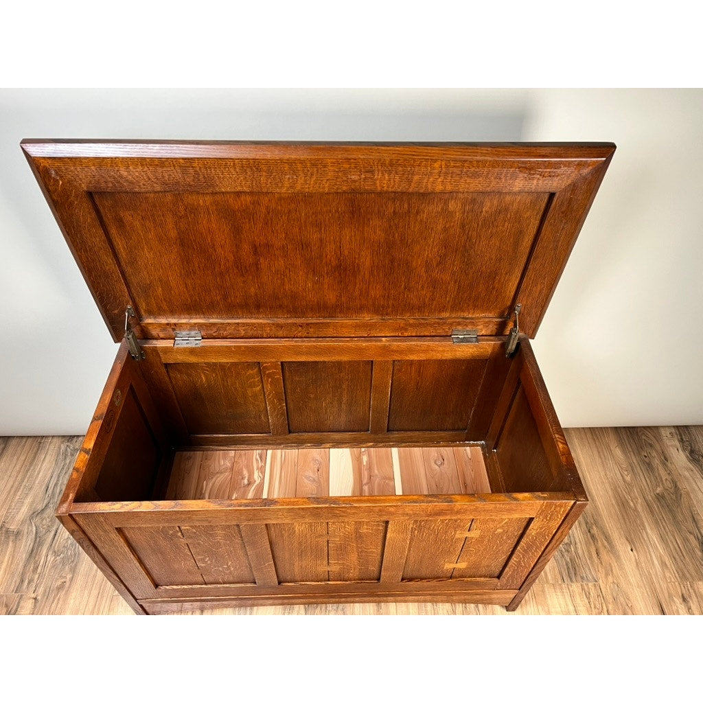 The Vintage Stickley Harvey Ellis Millennium Edition Oak Blanket Chest by Stickley features an open hinged lid, empty interior, paneled sides, and rich brown finish. It sits on a wood floor against a light-colored wall.