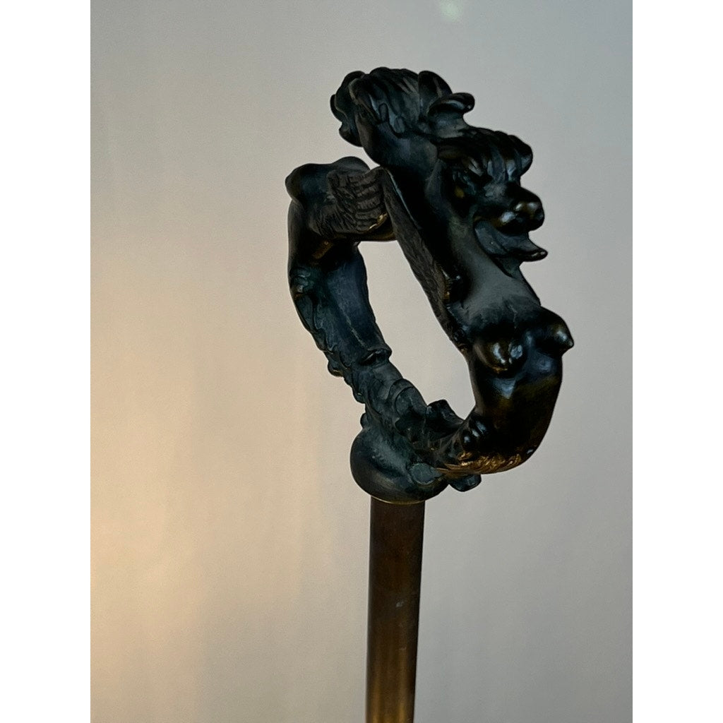 A dark metal cane handle shaped like a dragon's head and body forms a loop, attached to a straight rod, on a plain background—reminiscent of the ornate Antique Five Burner Lucerne Whale Oil Lamp with Napoleon I Fireplace Screen Shade.