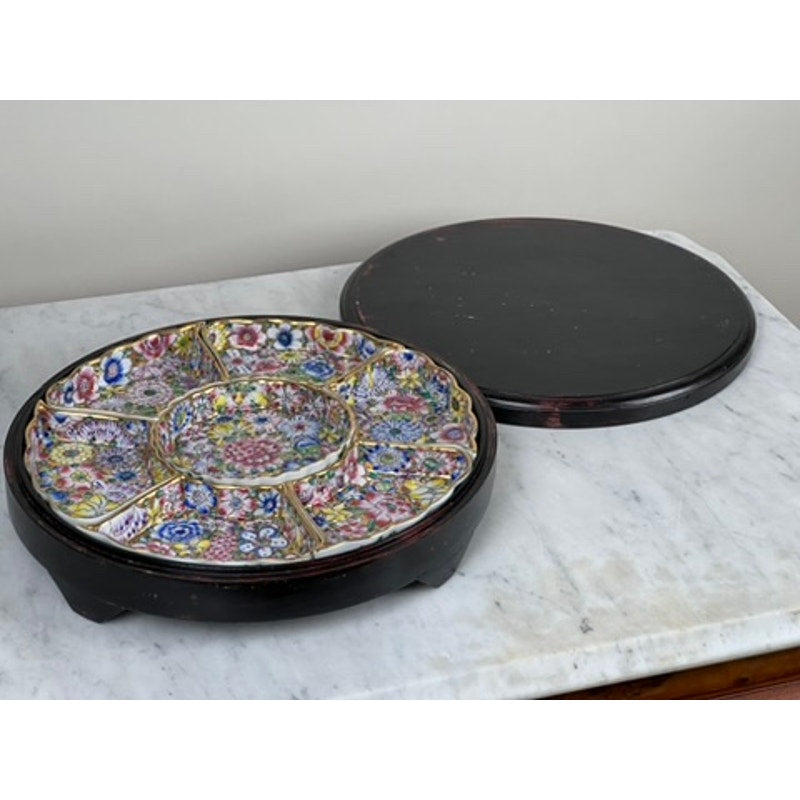 A Vintage Chinese Canton Sweet Meat Set with Case, c. Early 20th Century, featuring multiple round sections and colorful floral patterns, rests on a dark wooden tray beside a plain lid atop a white marble surface.
