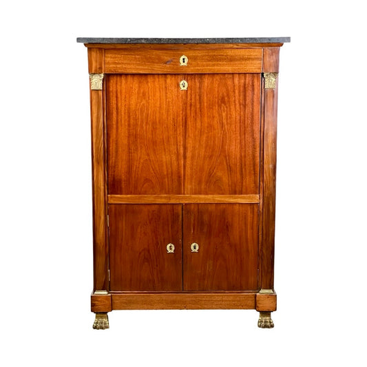 The Antique French Empire Secrétaire Abattant, mid 19th century, features mahogany veneer, a dark stone top, ormolu mounts on corners and feet, brass keyholes, a drop-down front panel above two cabinet doors.