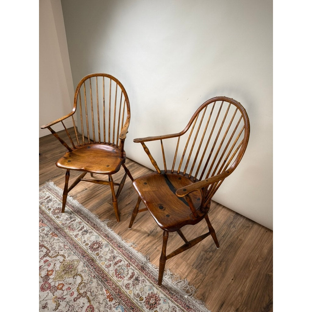 A Pair of Signed L.E. Partridge Connecticut Bench-Made Continuous-Arm Windsor Chairs, c. 1960s, featuring curved backs and spindles inspired by early American furniture, sit on a wood floor next to a patterned area rug against a plain light-colored wall.