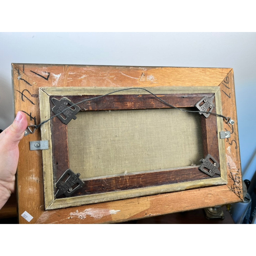 The image shows the back of an Antique American School Farmstead Landscape Oil Painting, Circa 1900, with metal brackets, hanging wire, handwritten markings, and numbers; a hand holds the frame. Brand is unknown.