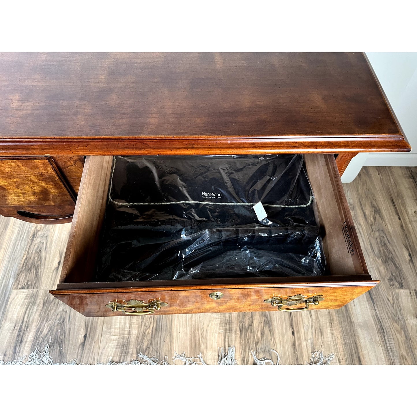 A wooden drawer with brass handles is pulled open, revealing a black felt-lined interior. The drawer belongs to the Henredon Vintage Solid Cherry Queen Anne Style Sideboard, shown on a wooden floor with a small rug edge visible.