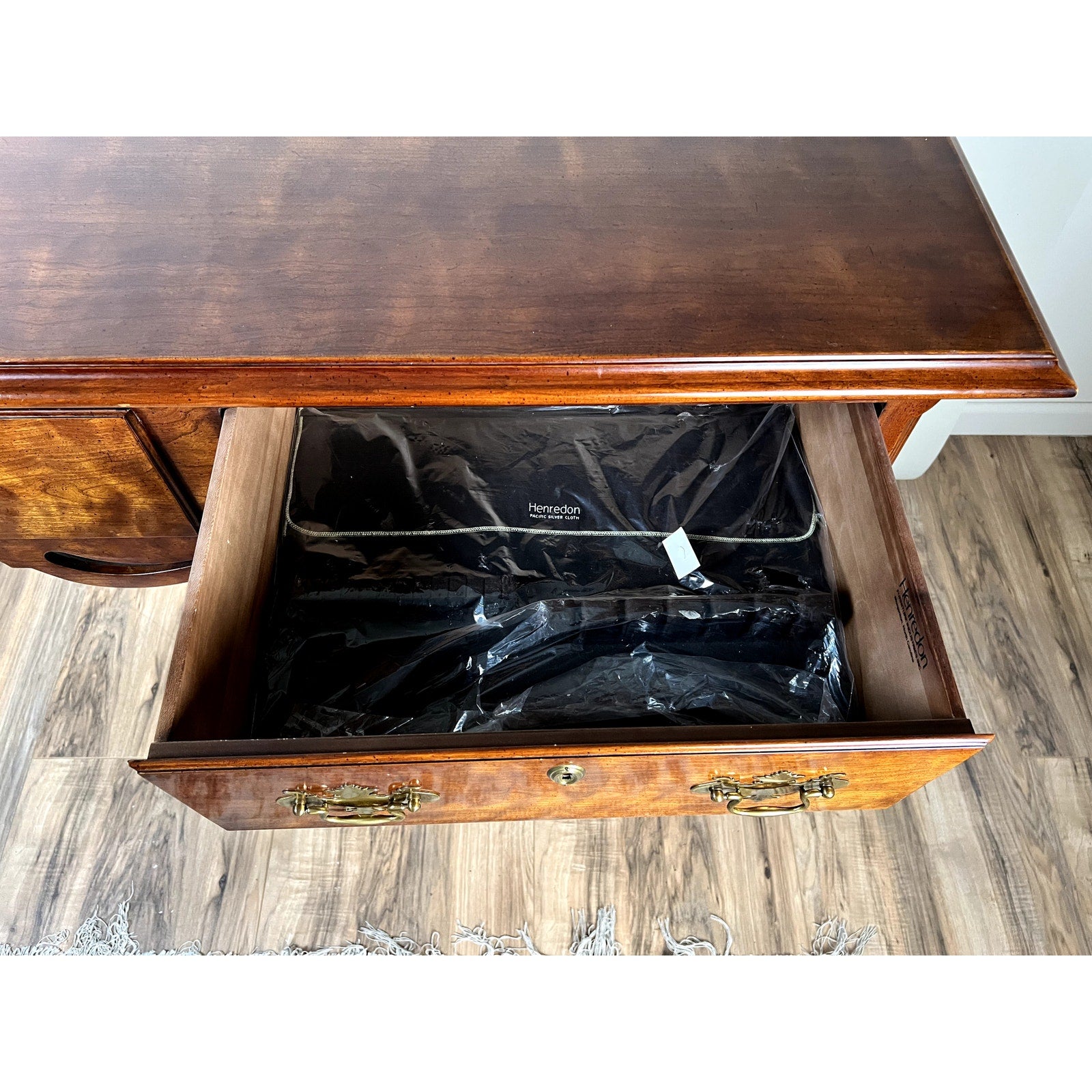 A wooden drawer with brass handles is pulled open, revealing a black felt-lined interior. The drawer belongs to the Henredon Vintage Solid Cherry Queen Anne Style Sideboard, shown on a wooden floor with a small rug edge visible.