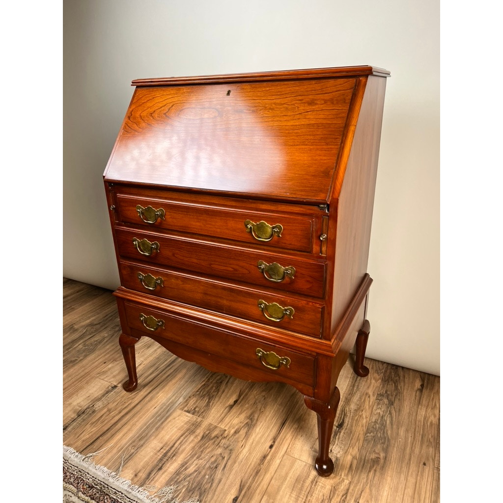 A Vintage Solid Cherry Queen Anne Style Slant Front Secretary Desk by Pennsylvania House, featuring four drawers with brass handles and curved legs, stands on a wood floor against a plain light-colored wall.