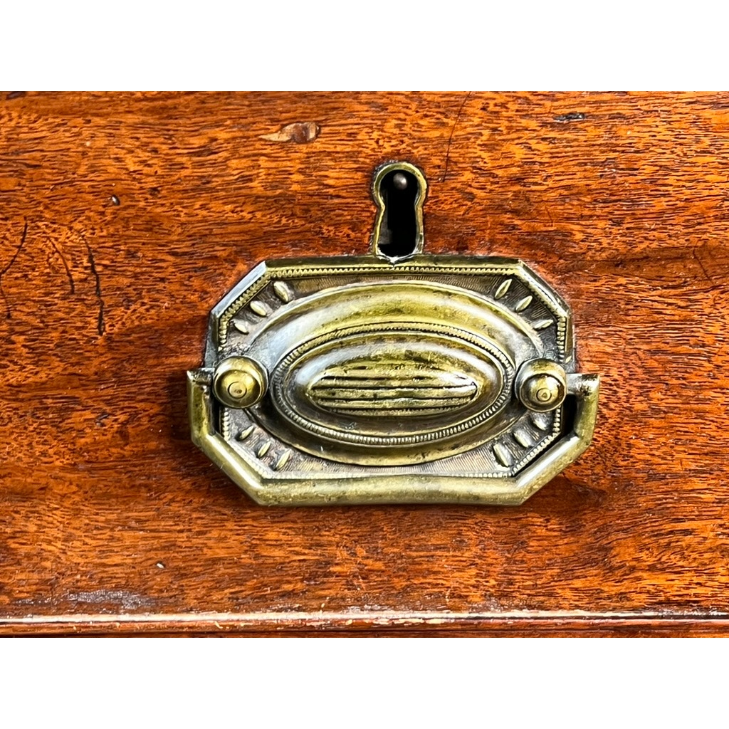 Close-up of an ornate brass drawer pull with an oval design, affixed to the rich reddish-brown mahogany of a Late Georgian English Chest of Drawers, Circa 1780–1810. A keyhole is positioned above the handle, recalling the refined craftsmanship and elegant aesthetic characteristic of period furniture from this era.