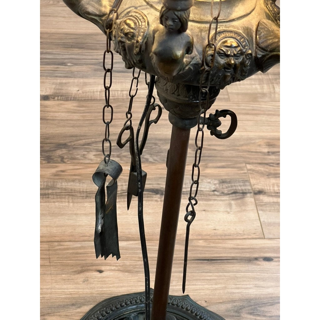 A close-up of an Antique Five Burner Lucerne Whale Oil Lamp with Napoleon I Fireplace Screen Shade, ornate stand, chains, and vintage iron keys/tools, set against a wooden floor background; brand: none/unknown.