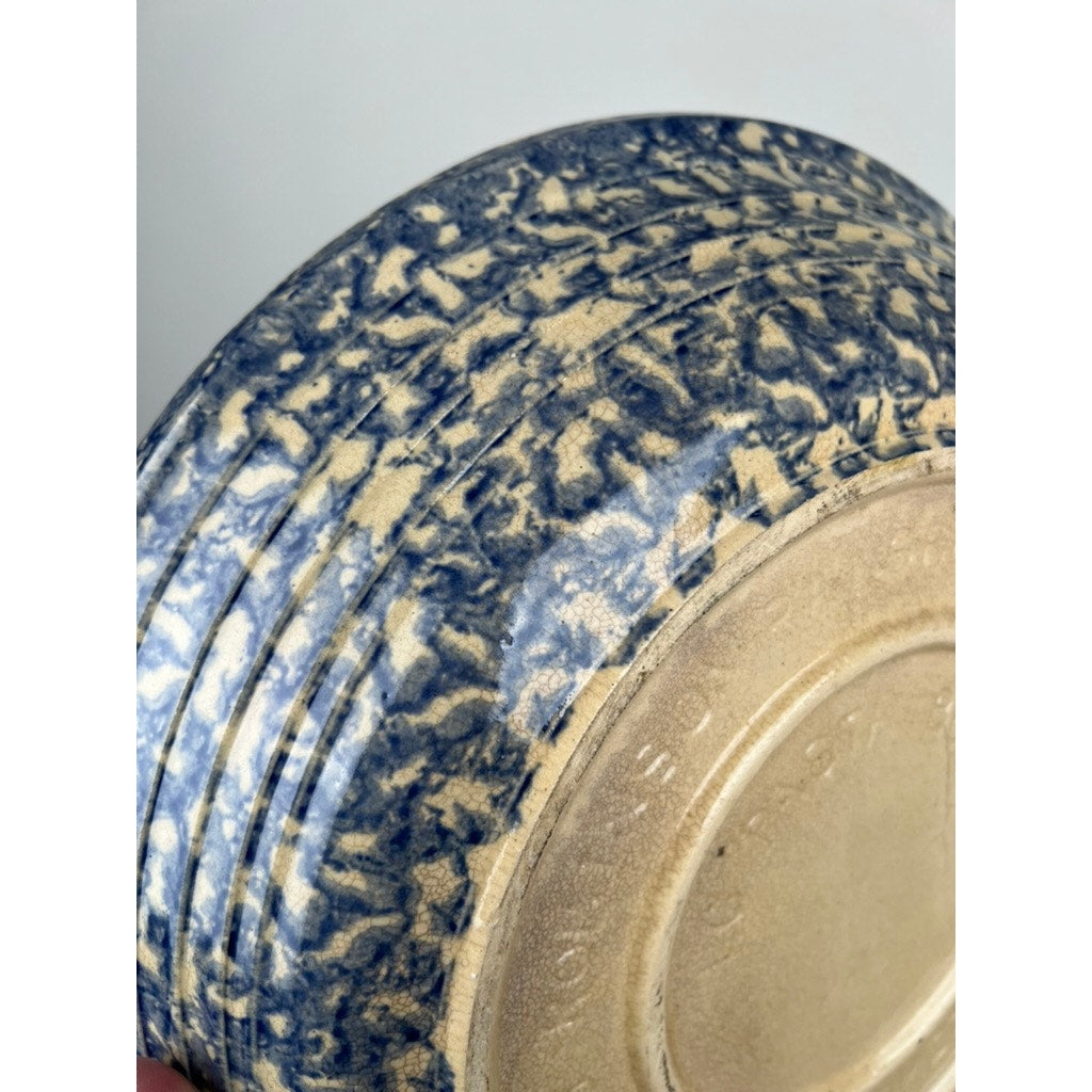 Close-up of the unglazed, textured base of a Robinson Ransbottom Roseville Blue Spongeware Pasta Bowl. The mottled blue and beige glaze features speckled patches and concentric rings, evoking classic American stoneware style.