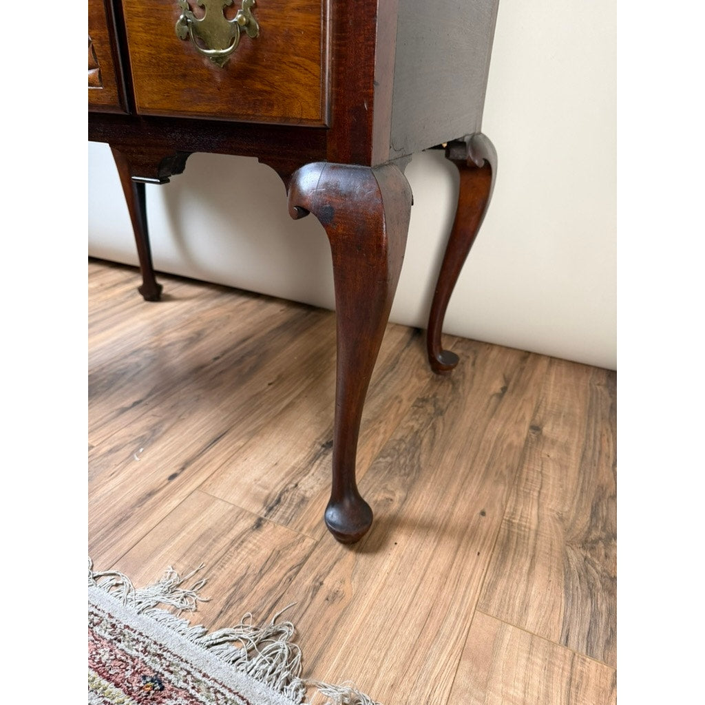 Close-up of the dark walnut cabriole legs on an 18th Century American Queen Anne Walnut Shell-Carved Lowboy, c. 1740–1770, standing on a wooden floor near the fringed edge of a patterned rug, with a plain light-colored wall in the background.