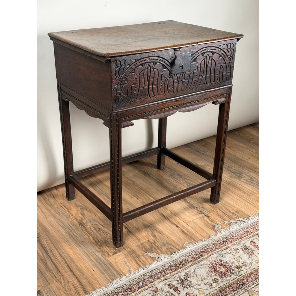 An English Jacobean Carved Oak Bible Box on Later Stand from the late 17th century, featuring an antique oak construction with an ornate carved front panel resting on a tall, four-legged stand.