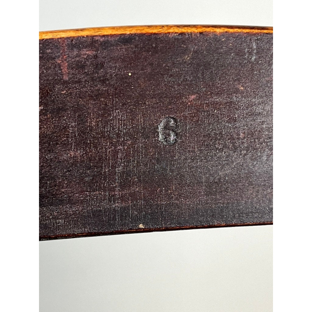 A close-up of the dark wood surface from an Antique Shaker #6 Tape Seat Rocker by Mt. Lebanon Shakers, late 19th century, shows a faintly stamped “6” in the center against an out-of-focus light grey background.