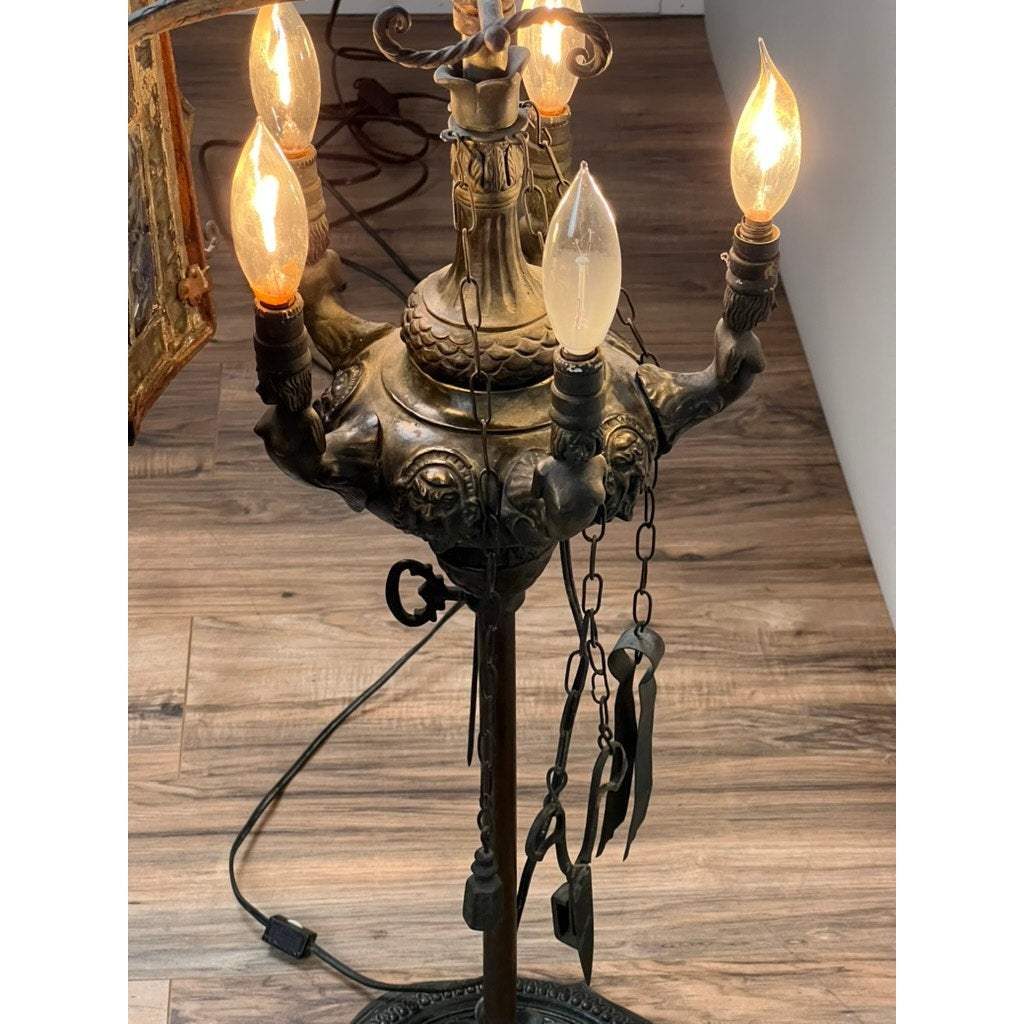 An Antique Five Burner Lucerne Whale Oil Lamp with a Napoleon I Fireplace Screen Shade, featuring ornate detailing and hanging metal chains, stands on a wooden floor and evokes the elegance of classic vintage design.