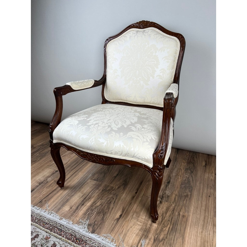 A Vintage Louis XV Style Fauteuil Arm Chair by Pennsylvania House, featuring ornate carved details and cream floral upholstery, sits on a wood floor near a patterned rug and a light gray wall.