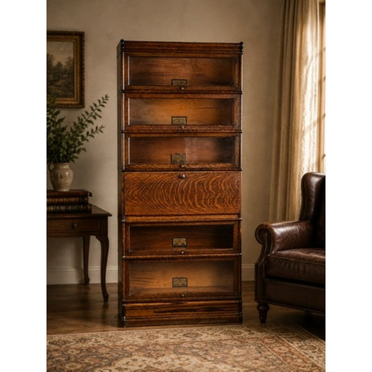 A tall Antique Globe-Wernicke Quarter Sawn Oak 6-Stack Barrister Bookcase Secretary Desk (c. 1905–1915) from Pearl City Antiques stands near a brown leather armchair and a side table in a warmly lit room with beige walls and curtains.
