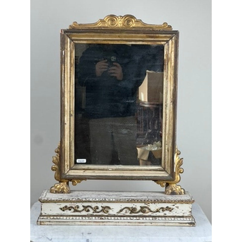 An Antique French Empire Gilt Wood Vanity or Table Mirror, c. mid-19th century, features a gilded frame and carved neoclassical details. The mirror reflects a person taking a photo and background furniture, highlighting its vintage charm.