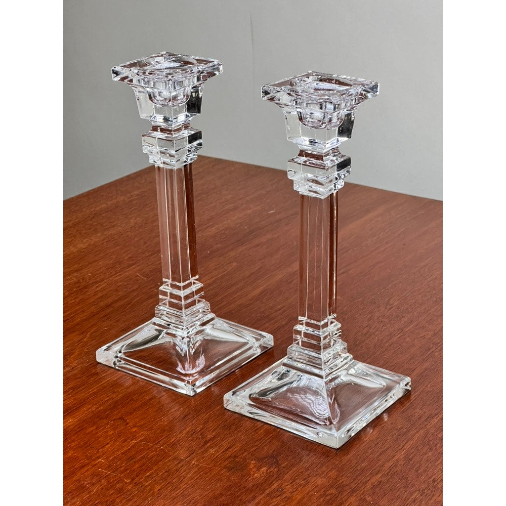 A Vintage Pair Tiffany & Co. Clear Crystal Candlesticks by Tiffany & Co. with square bases and geometric details are displayed on a wooden surface against a plain gray background.